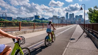 People on bike share bikes on bridge with Minneapolis, Minnesota skyline in background