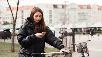 Woman stands next to a bike with one hand on handlebar holding her mobile phone.