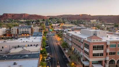 Aerial view of wide street in St. George, Utah at dusk with red rock mountains in background.