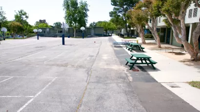 View of empty paved schoolyard with green picnic benches and basketball hoops in Malibu, California