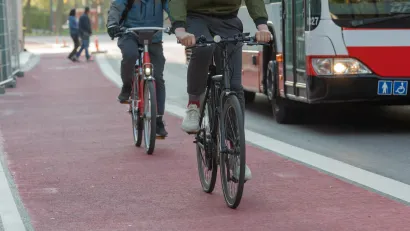 Two people on bikes in red painted bike lane with bus in traffic lane next to them.