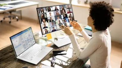Woman at desk with laptop and extra monitor with Zoom session open.