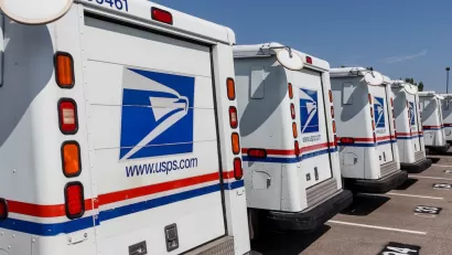 Row of USPS trucks parked in outdoor parking lot.