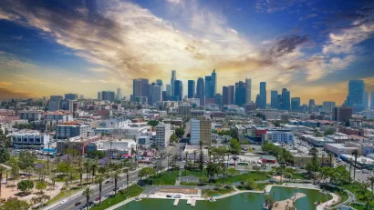 Aerial view of Macarthur Park lake with downtown Los Angeles skyline in background.