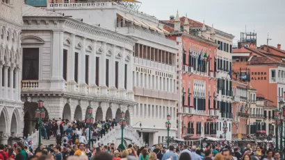 Line of colorful historic buildings on one side of a square jammed packed with people.