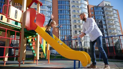 Man reaching for young girl sliding down playground slide.