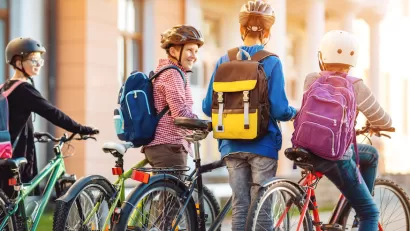 Group of four children with backpacks and helmets riding and walking their bikes.