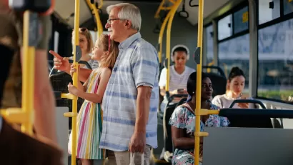 Elderly man and granddaughter standing on public bus.