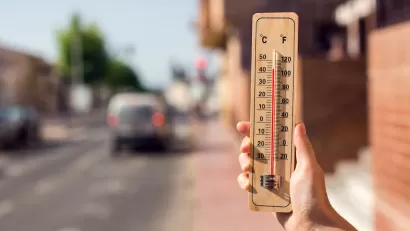 Close-up of hand holding up wooden thermometer in front of blurred street