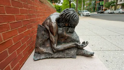 Bronze statue of homeless man (Jesus) with head down and arm outstretched in front of St. Matthew Cathedral in Washington D.C.