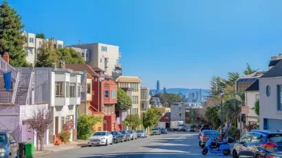View down San Francisco street with colorful residential buildings and high-rise downtown buildings in distance.