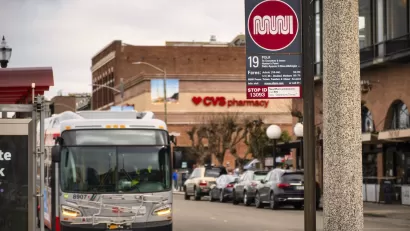 Close-up of white and red Muni sign at bus stop on Polk Street in San Francisco, California with blurred bus in background.