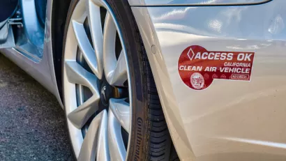 Close-up of maroon California 'Clean Air Vehicle' carpool lane access sticker on the back bumper of a silver Tesla vehicle.