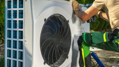 Close-up of worker installing white electric heat pump outdoors.