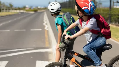 Two young boys wearing bike helmets looking right before crossing the street on their bicycles