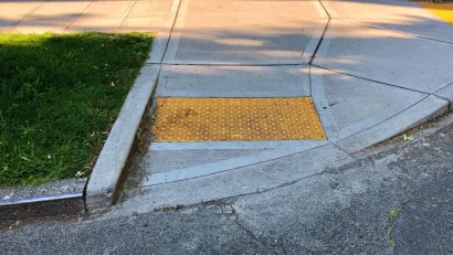 Curb cut at corner of sidewalk with yellow panel with bumps to indicate wheelchair ramp.