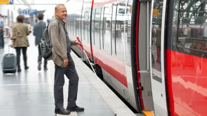 Man using cane for visual impairment waiting to board subway train on platform.
