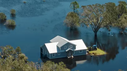 A gray hope with white roof surrounded by floodwaters that come up just above the home's foundations.