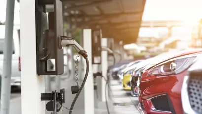 Close-up of red car parked and plugged in at EV charging station with row of cars behind it.