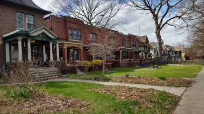Row of older brick houses in Detroit with front porches and front lawns.