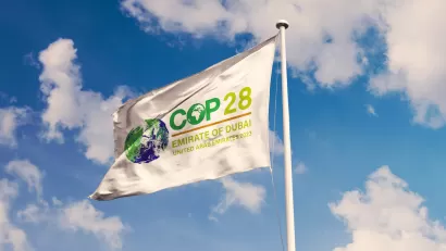 White flag with COP28 cliamte conference logo against lightly cloudy blue sky.