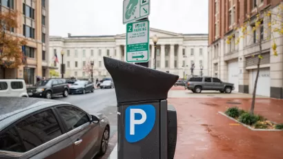 Electronic parking pay station next to curb in Washington D.C., on rain-soaked red brick sidewalk with neoclassical white building in background