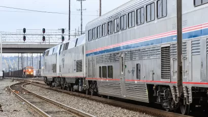 Silver and blue Amtrak train approaching an oncoming orange freight train at station in Seattle, Washington.