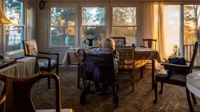 Senior woman sitting inchair looking out large window at golden hour in Broomes Island, Maryland.