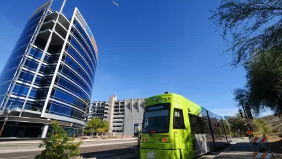 Green Tempe streetcar with downtown Tempe glass building in background.