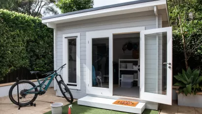 Small gray backyard cottage with glass door and bike sitting in front of it