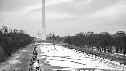 National Mall in winter with snow and people walking around, Washington Monument obelisk visible in background.