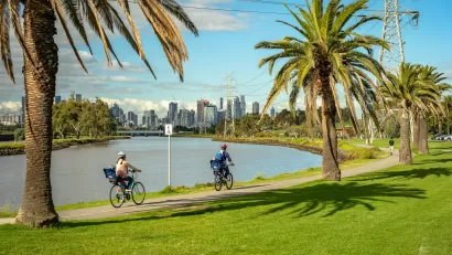 Two people on bikes on a riverbank trail in Melbourne, Australia with city skyline in background