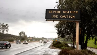Freeway sign with "severe weather - use caution" over multilane freeway in rainy weather.