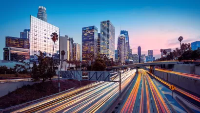 Blurred traffic speeding by on freeway with Los Angeles skyline in background.