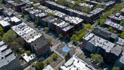 Aerial view of intersection in Hoboken, New Jersey with crosswalks, bulb-outs, and blue home plate painted in middle of intersection, surrounded by mid-rise multistory apartment buildings.