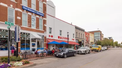Main Street in Bentonville, Arkansas with three-story brick buildings, people sitting at tables on sidewalk, and sign on building for "The Walmart Museum."