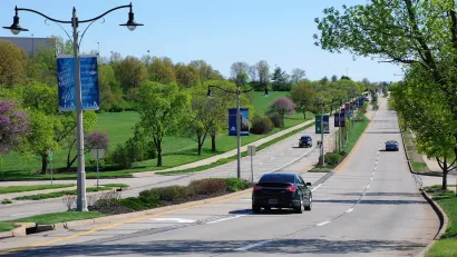 Wide suburban road with landscaped median and light pole banners advertising local amphitheater.