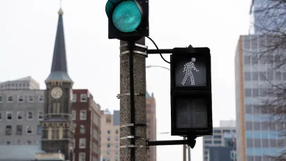 Close-up on pedestrian crosswalk light in downtown Milwaukee, Wisconsin with historic building with steeple visible in background.