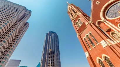 View up at brick Catholic church towers and modern high-rise buildings.