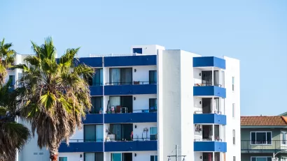 Top floors of blue and white apartment building with palm trees against sunny blue sky in Malibu, California.