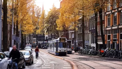 Tram and cyclist on Amsterdam street with sunrise or sunset in background.