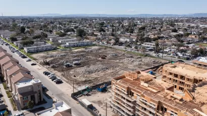Aerial view of large construction site and vacant, graded lot next to public housing buildings in Watts, Los Angeles, California.