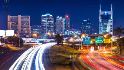 View of Nashville skyline at night with blurred highway lights in foreground.
