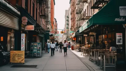 View of New York City alleyway with outdoor restaurant seating and people walking between brick apartment buildings with fire escapes