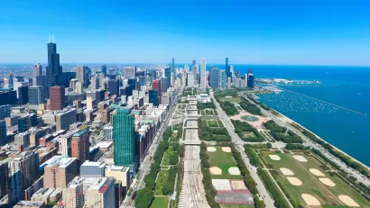 Aerial view of the Chicago Loop in summer from the south, with buildings on the left, Grant Park in the center, and Lake Michigan on the right.