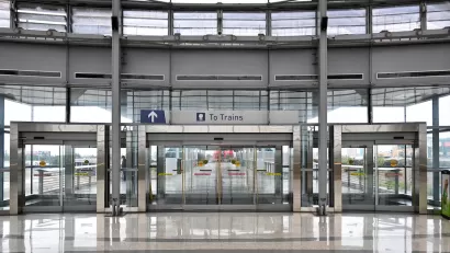 View of large glass building with glass doors and "To Trains" sign.