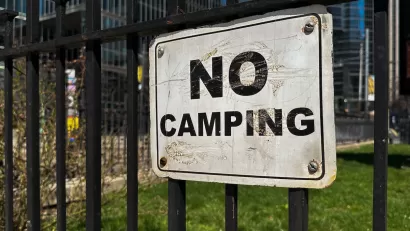 Close-up of white and black NO CAMPING sign on black iron fence.