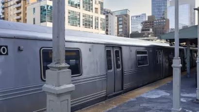 Silver train at station on elevated track with city high-rises in the background.