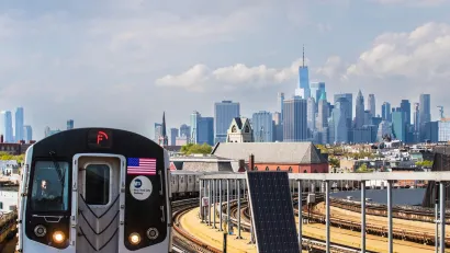 NYC MTA train on elevated rail with Manhattan skyline visible in background.