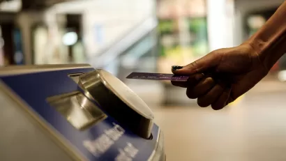 Close-up of hand holding transit card up to fare collection machine in transit station.